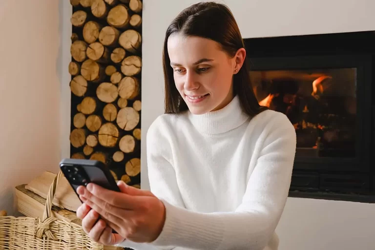 A woman at the fireplace looking up fireplace terminology on her phone.